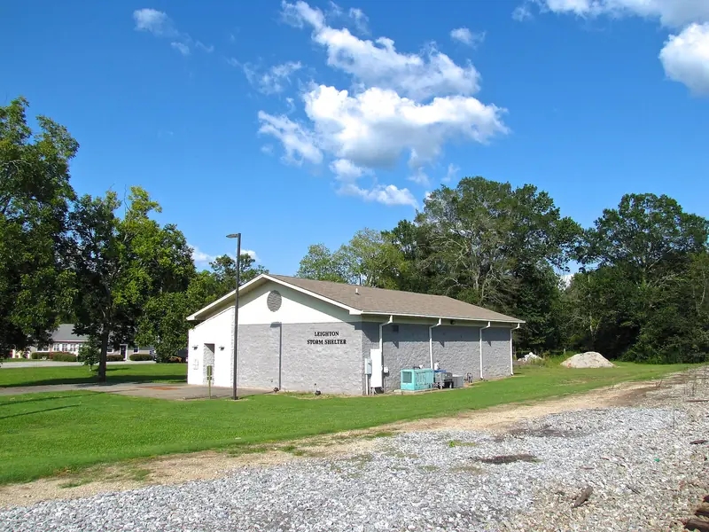 A single-story concrete block community storm shelter on a lawn under a blue sky