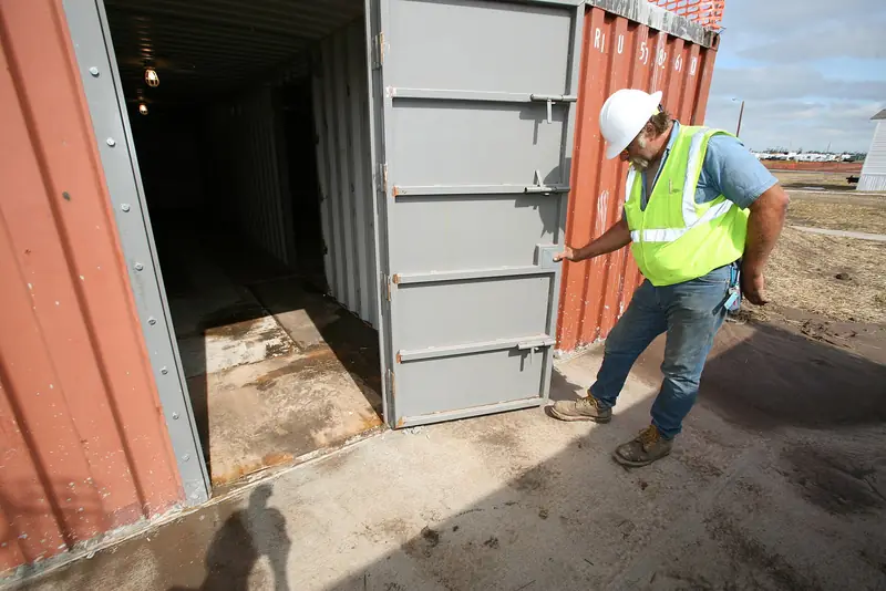 A contractor in a hard hat and safety vest checks the steel door of a new storm shelter