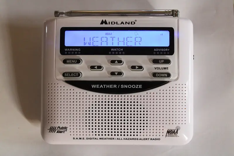 A white NOAA weather alert radio with a small display reading WEATHER